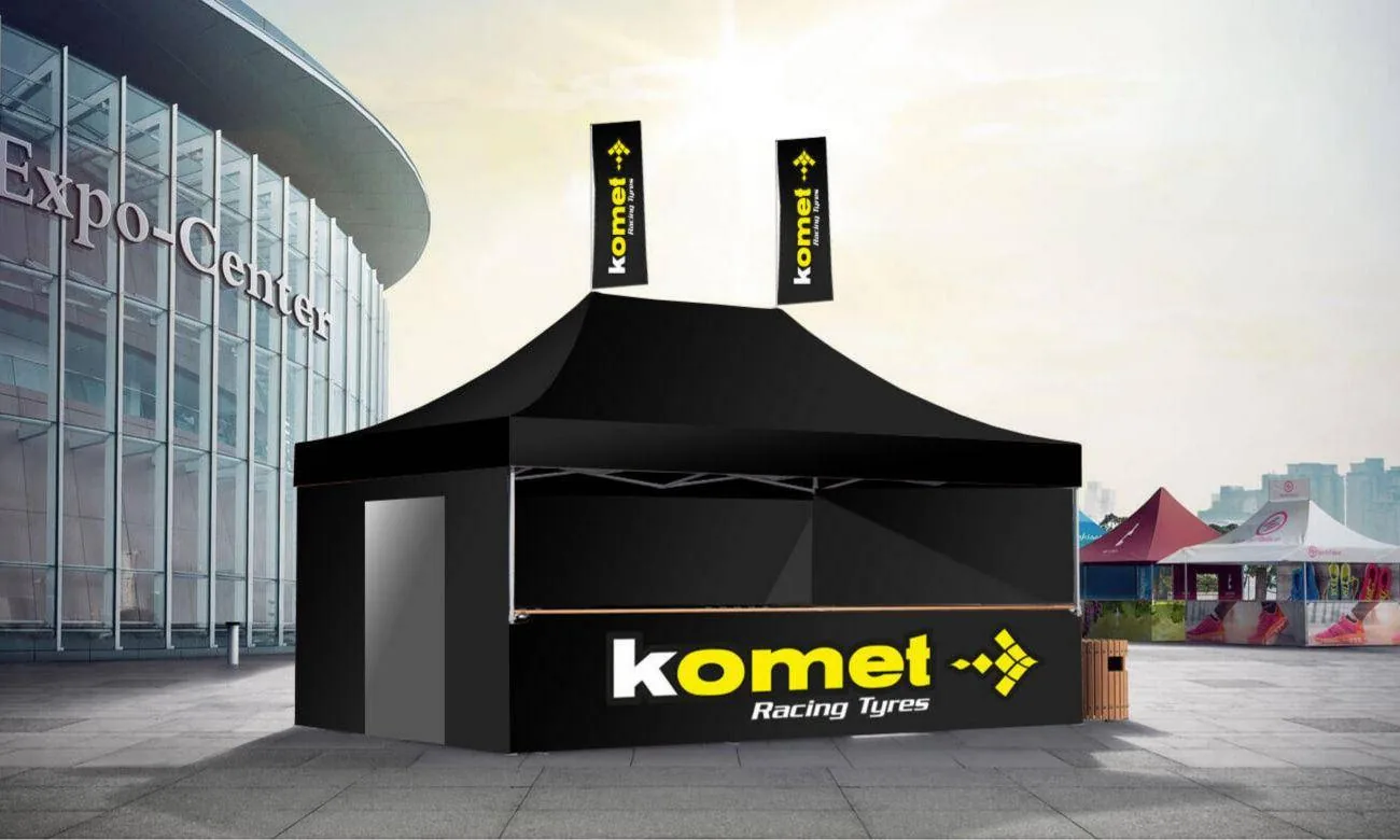 The Komet Mastertent: black gazebo with yellow Komet branding, counter and two flags